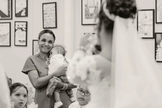 En noir et blanc, une femme tient un bébé parmi des enfants, près du voile de la mariée