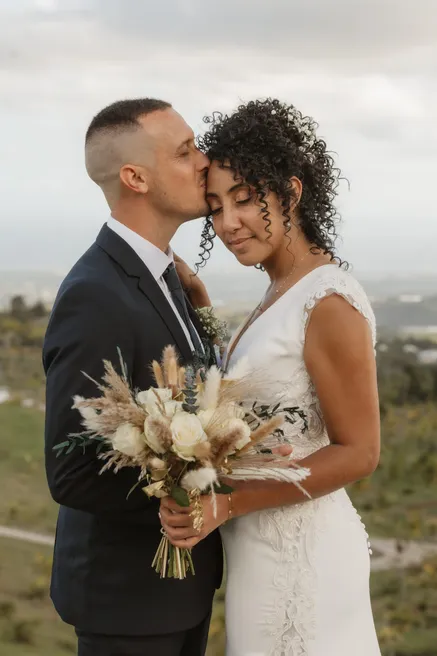 Le marié embrasse le front de la mariée, bouquet de fleurs séchées entre eux, au-dessus des collines