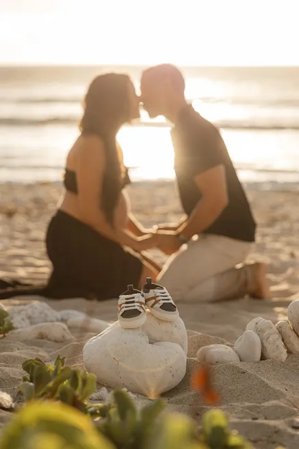 Un couple à genoux sur le sable s’embrasse face au soleil, petits chaussons au premier plan