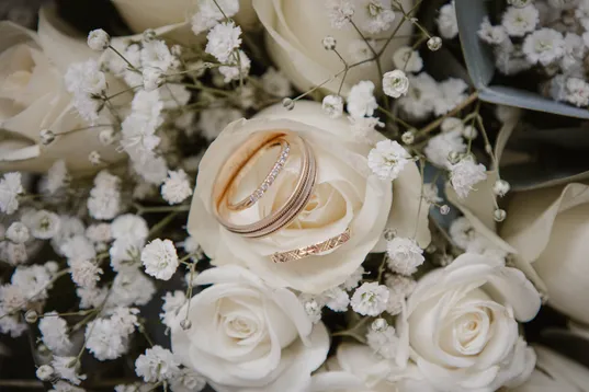 Deux alliances posées sur une rose blanche, entourées de gypsophile et de roses