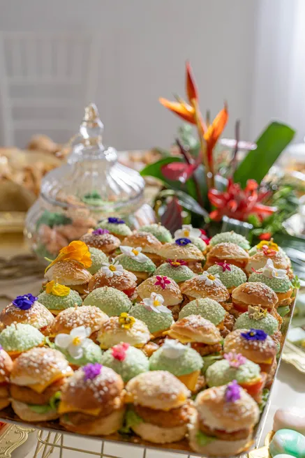 Plateau de mini-burgers décorés de fleurs comestibles, près d’un bouquet d’oiseaux de paradis