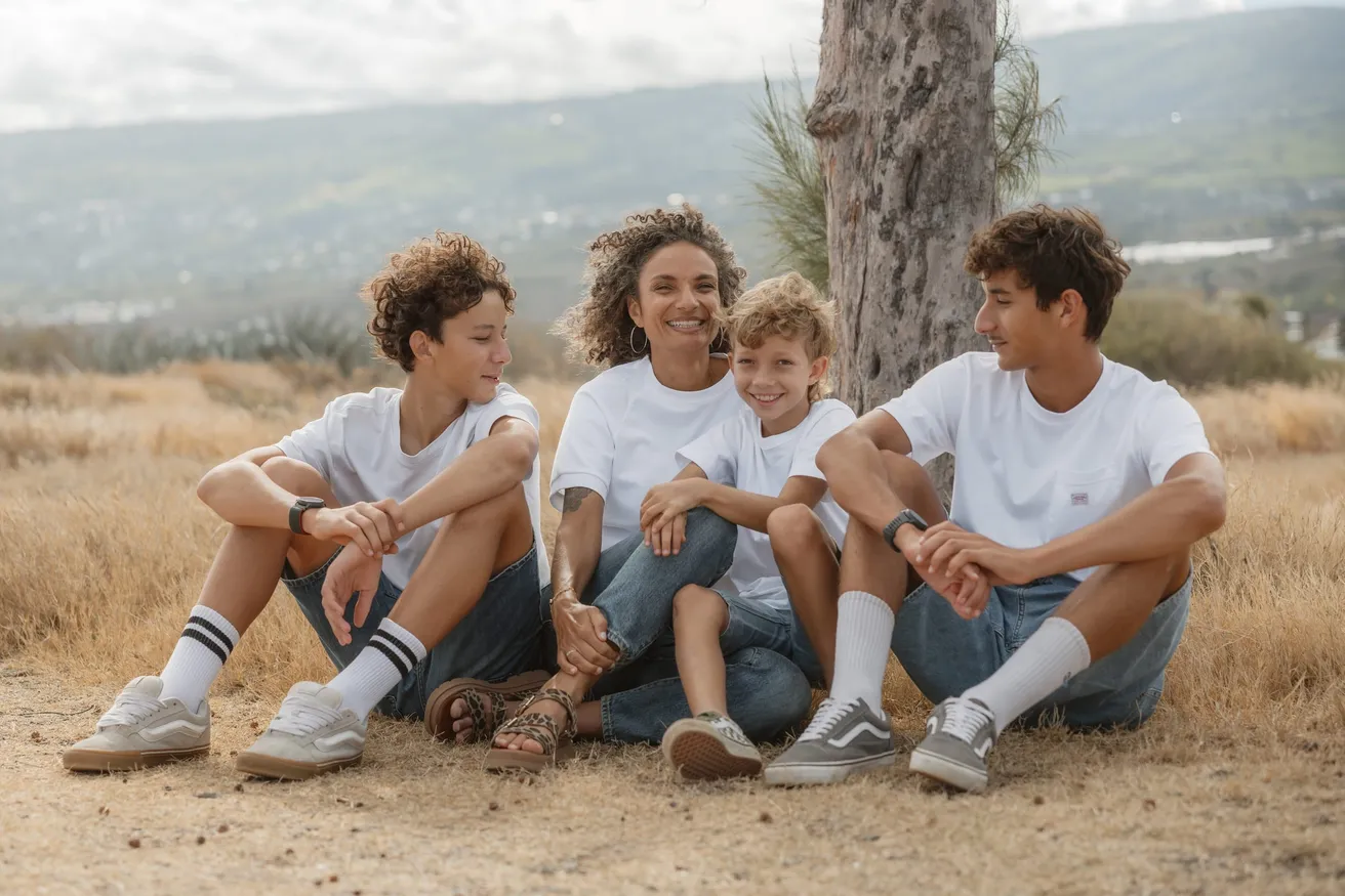 Une mère et ses trois fils en tee-shirts blancs assis dans les herbes sèches, la mer au loin