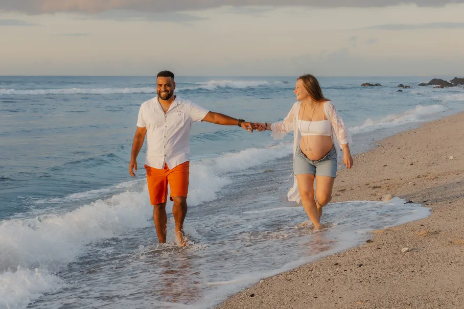 Un couple marche main dans la main dans les vagues, sous un ciel bleu