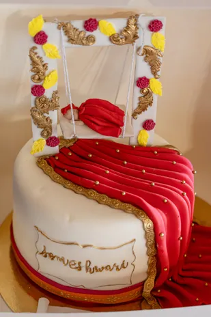 Un gâteau blanc en forme de berceau, drapé de tissu rouge et orné de dorures