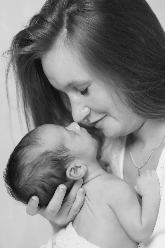 En noir et blanc, une maman contemple son nouveau-né qu’elle tient contre elle