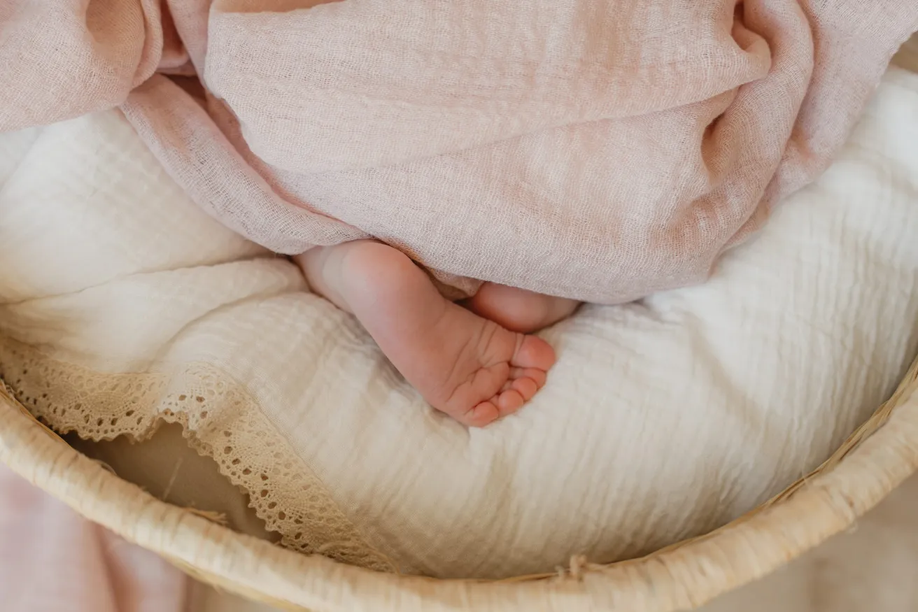 Les petits pieds du nouveau-né dépassent d’un lange rose, dans un panier tressé garni de coton