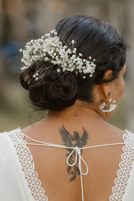 Chignon de la mariée orné de gypsophile, vu de dos, sur une robe au dos ouvert bordé de dentelle