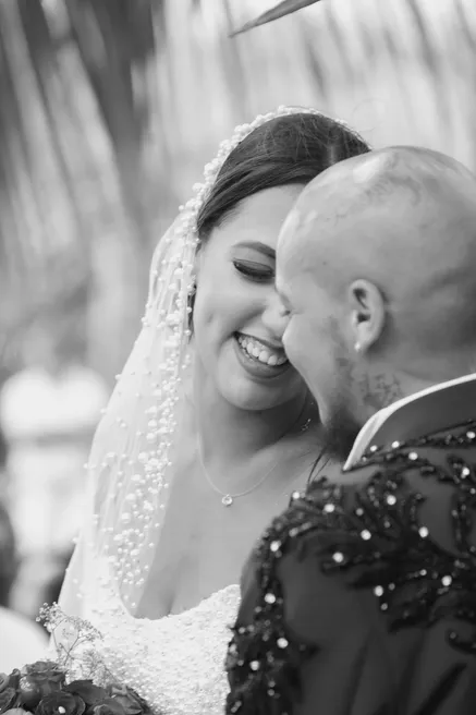 En noir et blanc, la mariée rit sous son voile de dentelle, joue contre joue avec le marié