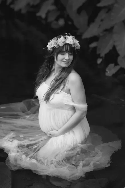 En noir et blanc, future maman assise dans l’eau, la robe étalée autour d’elle