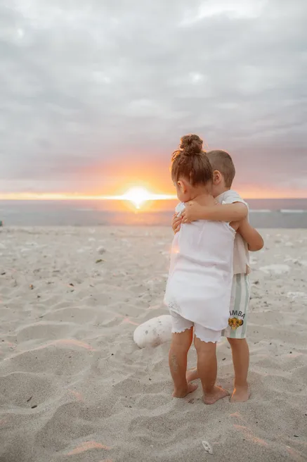 Deux enfants enlacés sur le sable, devant le soleil qui se couche