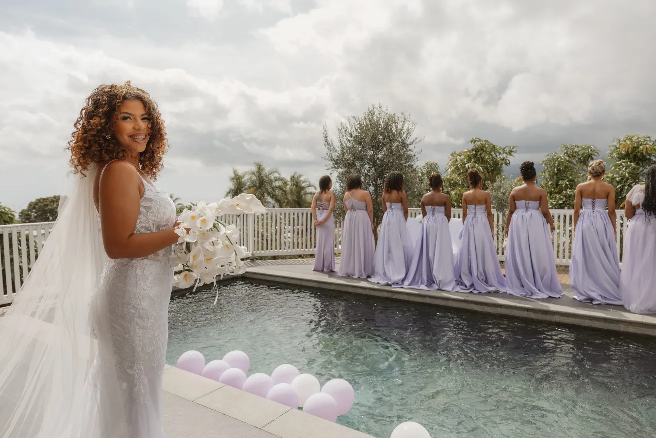 La mariée pose au bord d’une piscine, ses demoiselles d’honneur en lilas alignées au fond