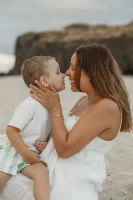 Une mère tient le visage de son petit garçon et l’embrasse, nez contre nez sur la plage
