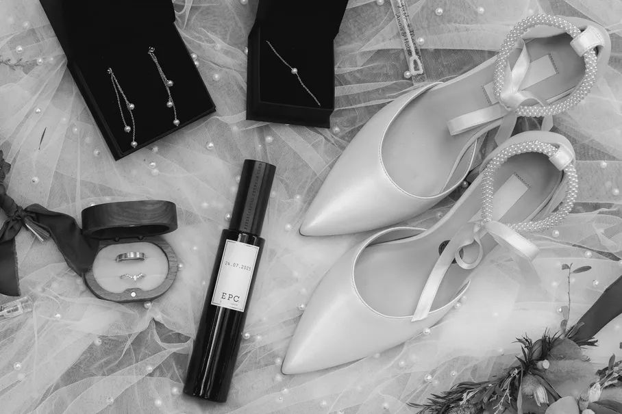 En noir et blanc, escarpins, boucles d’oreilles, parfum et écrin à alliance posés sur un voile