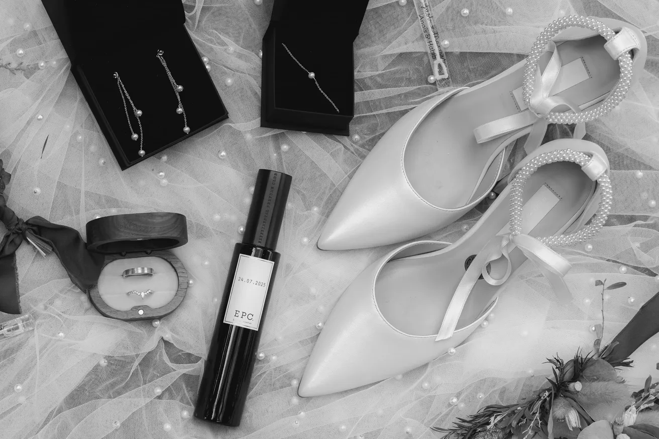 En noir et blanc, escarpins, boucles d’oreilles, parfum et écrin à alliance posés sur un voile
