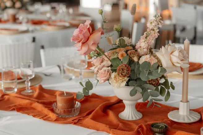 Centre de table de roses et d’eucalyptus dans une coupe blanche, sur un chemin de gaze orange