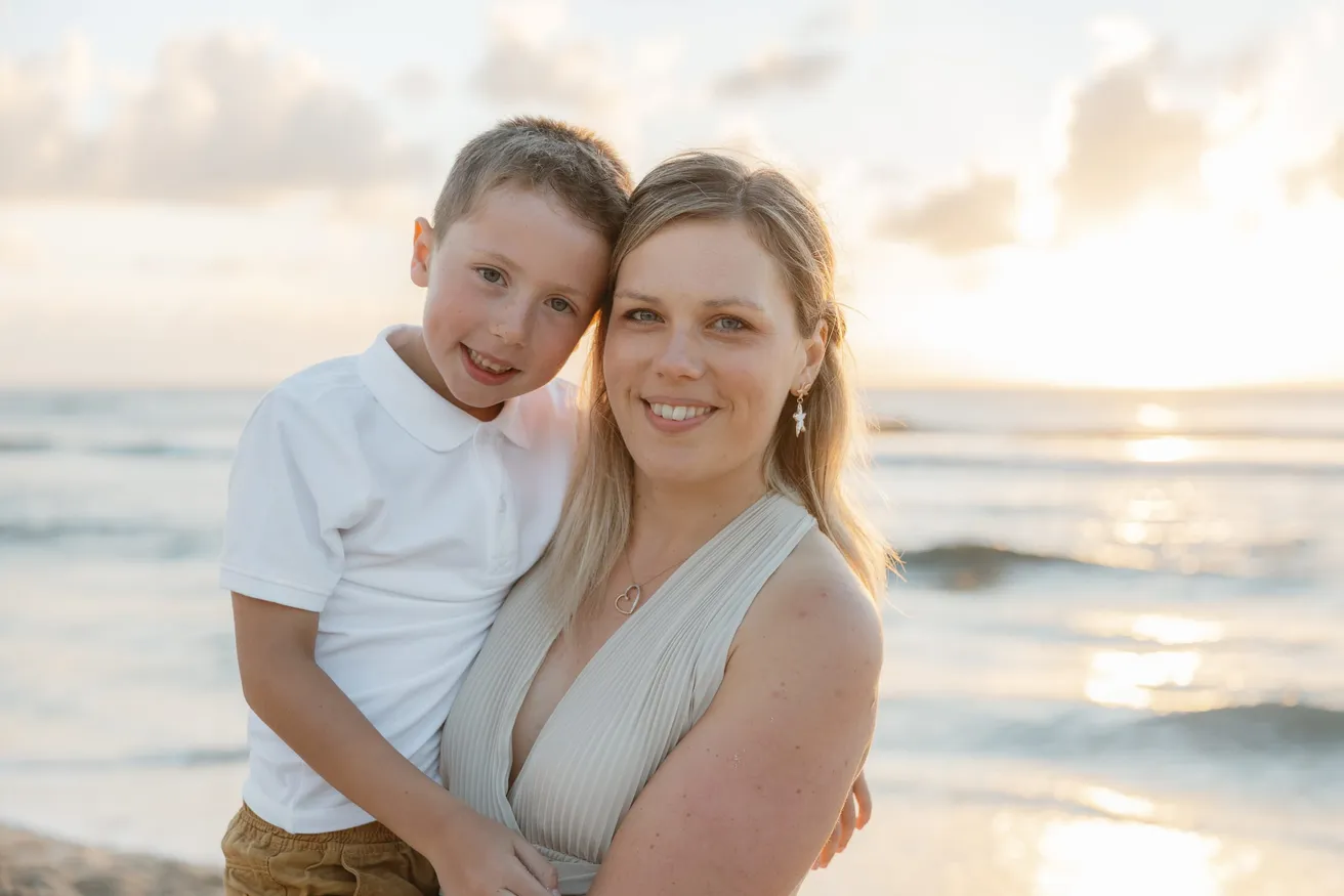 Une mère et son fils posent joue contre joue, devant la mer au soleil couchant