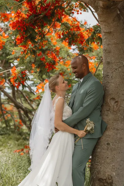 Les mariés enlacés contre un tronc, sous les fleurs orange d’un flamboyant