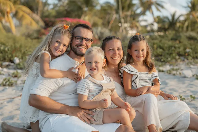 Les parents et leurs trois enfants blottis ensemble sur le sable, devant la végétation