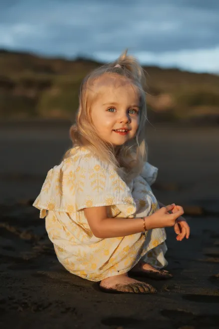 Une petite fille en robe jaune, accroupie sur le sable noir