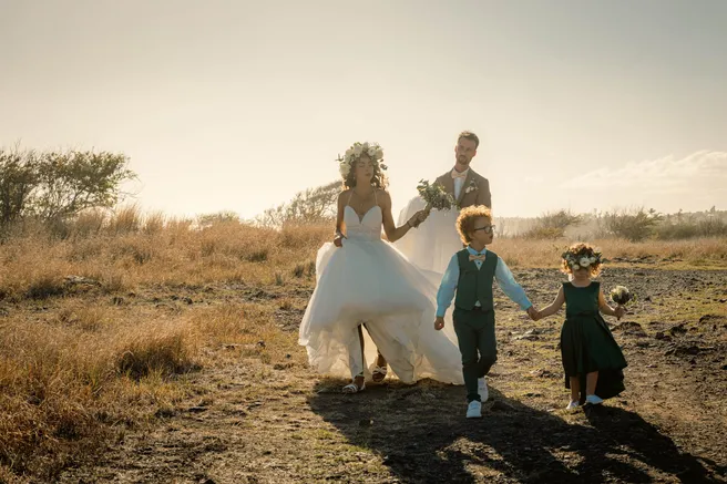 Les mariés marchent dans les herbes sèches au soleil couchant, main dans la main avec deux enfants