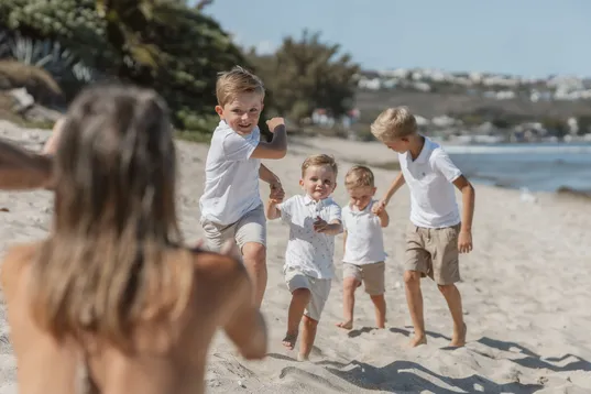 Quatre petits garçons courent sur le sable vers une femme floue au premier plan