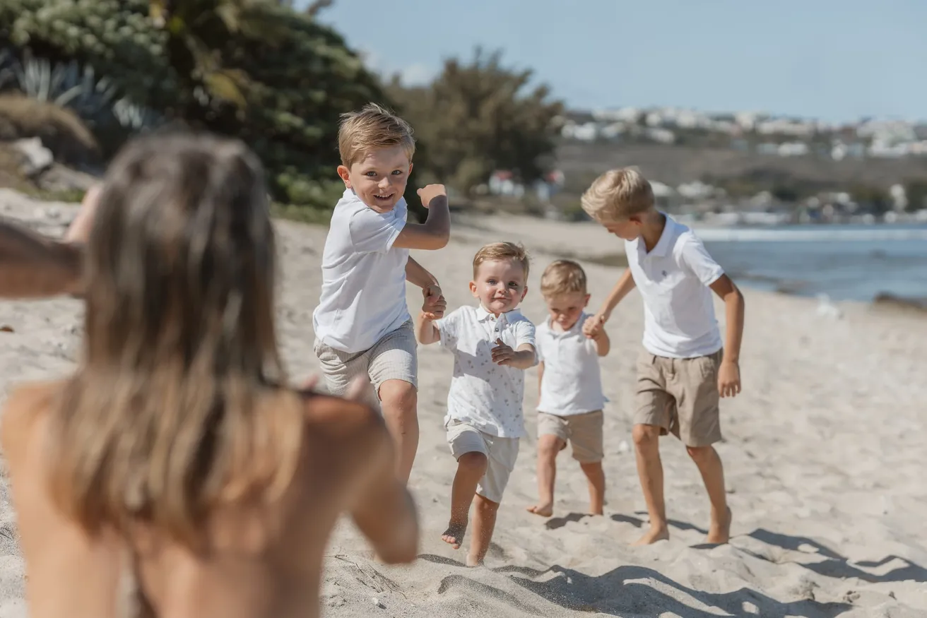 Quatre petits garçons courent sur le sable vers une femme floue au premier plan