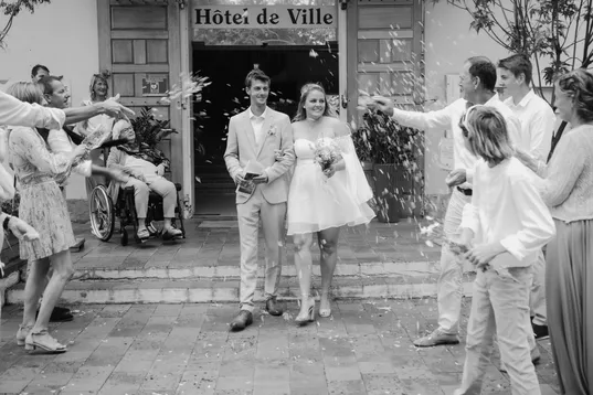 En noir et blanc, les mariés sortent de la mairie sous les pétales lancés par les invités