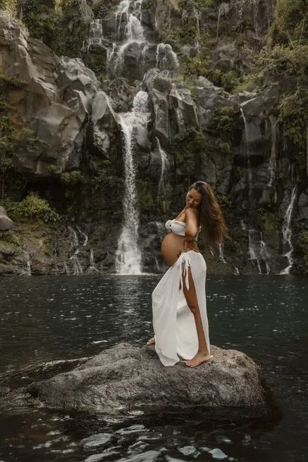 Future maman de profil sur un rocher au milieu du bassin, face aux cascades
