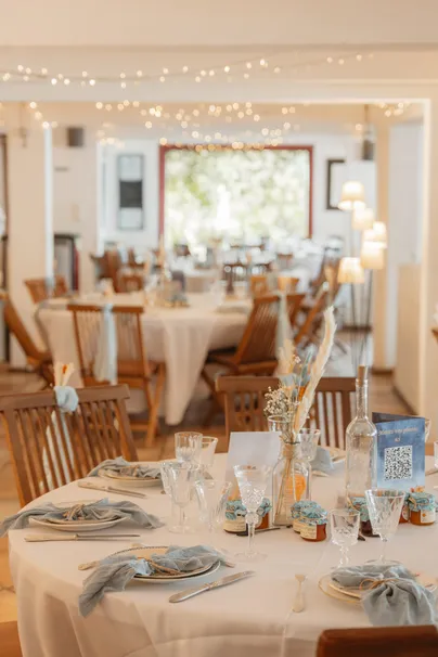 Salle de réception aux tables rondes, guirlandes lumineuses et petits pots de confiture