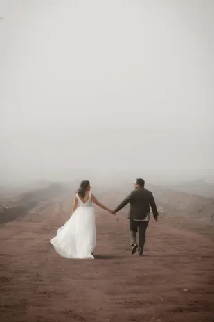 De dos, les mariés s’éloignent main dans la main sur une piste de terre rouge noyée de brume
