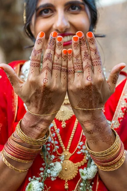 La mariée montre ses mains ornées de henné, ongles orange et bracelets dorés aux poignets
