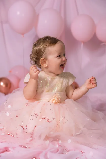 Une petite fille en robe de tulle rose rit aux éclats, assise devant les ballons roses