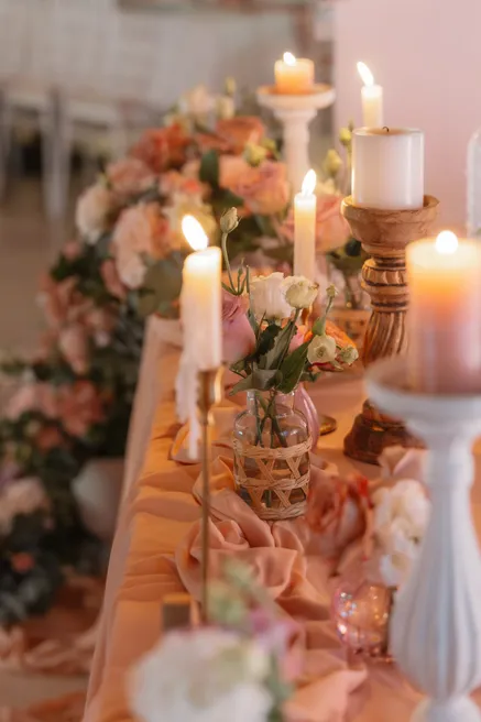 Table de réception garnie de bougies blanches, de chandeliers et de fleurs rose pêche