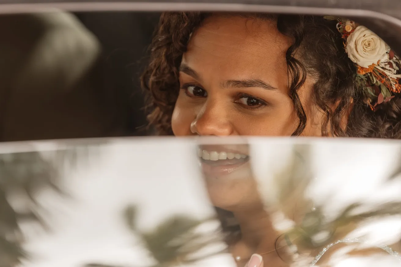 Le visage souriant de la mariée, fleurs dans les cheveux, aperçu par la vitre d’une voiture