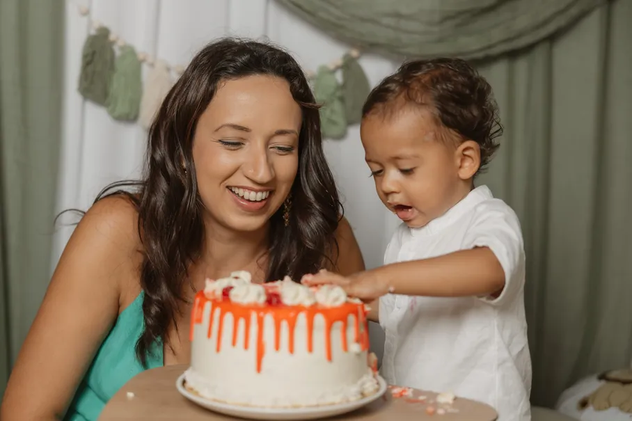 Une maman rit pendant que son petit garçon en chemise blanche goûte la crème du gâteau orange