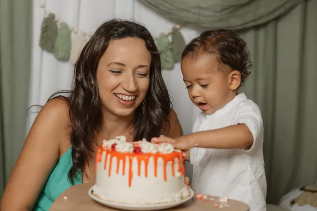 Une maman rit pendant que son petit garçon en chemise blanche goûte la crème du gâteau orange