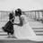 La mariée embrasse une petite fille sur un ponton, en noir et blanc