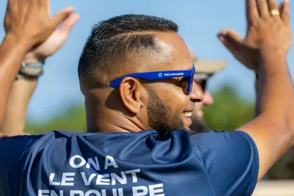 Un homme en tee-shirt « On a le vent en poulpe » et lunettes de soleil tape dans les mains de ses coéquipiers