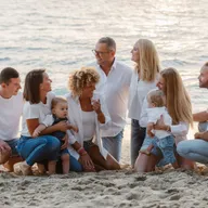 Une famille rit, assise sur le sable au bord de mer