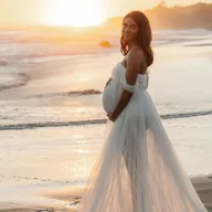 Future maman en robe blanche, souriante, au coucher du soleil